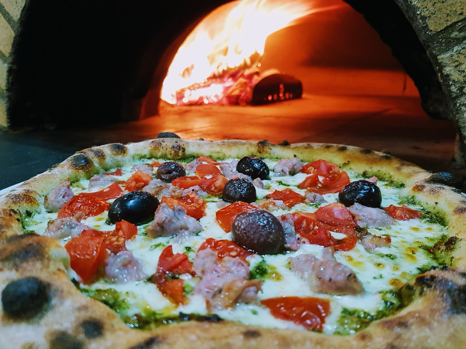 Pizza appena sfornata davanti al forno a legna acceso